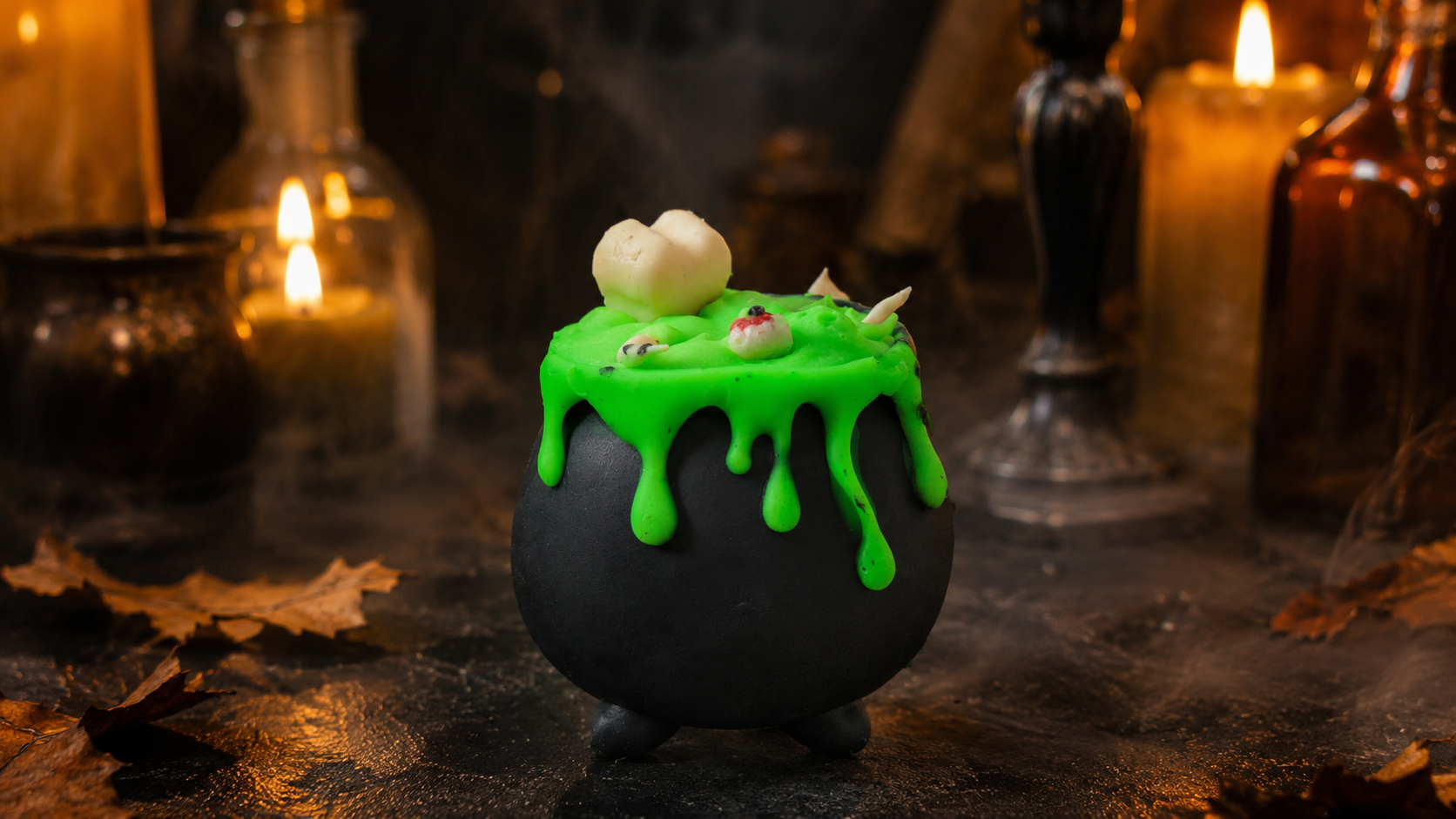 Savon artisanal Les Mels en forme de chaudron de sorcière noir, débordant de potion verte avec os et yeux, sur décor d'apothicaire aux chandelles